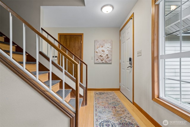 foyer with stairway, baseboards, and light wood finished floors