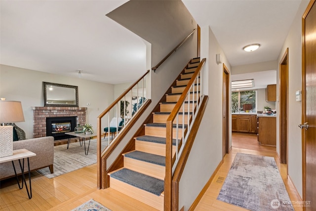 staircase with a brick fireplace, baseboards, and wood finished floors