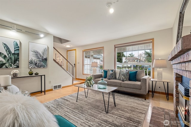 living room featuring visible vents, baseboards, stairway, a fireplace, and wood finished floors