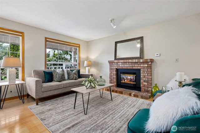 living area with baseboards, a brick fireplace, and light wood finished floors