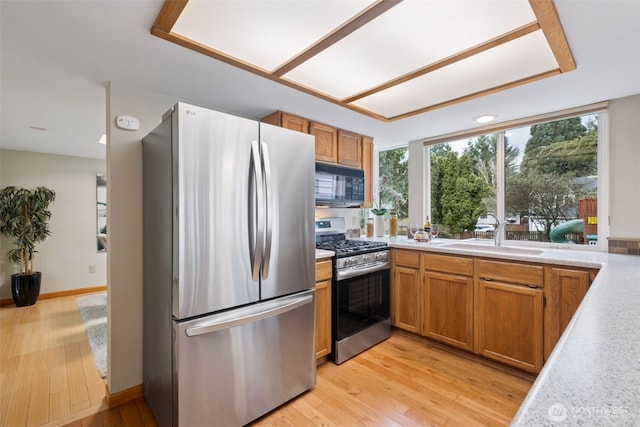 kitchen with a sink, light wood-type flooring, appliances with stainless steel finishes, and light countertops