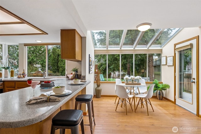 kitchen with light wood-type flooring, light countertops, brown cabinets, a kitchen breakfast bar, and a skylight