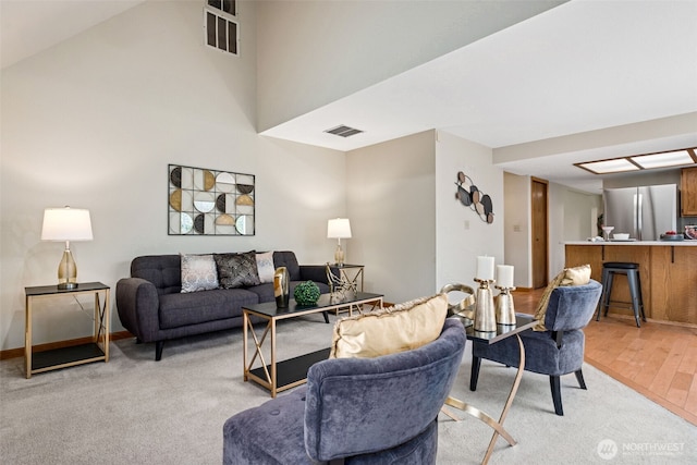 living room featuring visible vents, baseboards, a high ceiling, and light wood-style flooring