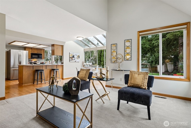 living area with vaulted ceiling with skylight, light colored carpet, visible vents, and baseboards