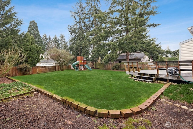 view of yard featuring a wooden deck, a playground, and a fenced backyard