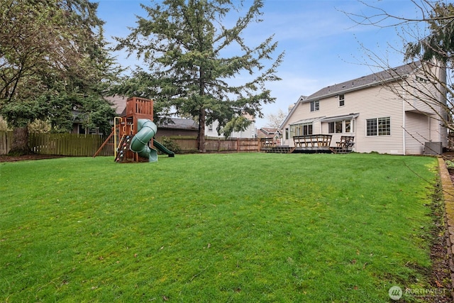 view of yard featuring a deck, a playground, and a fenced backyard