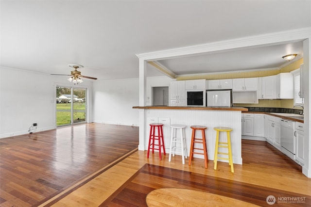 kitchen featuring dark countertops, dishwasher, a breakfast bar area, white cabinets, and fridge