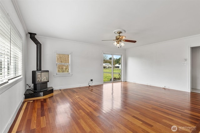 unfurnished living room featuring a ceiling fan, wood finished floors, a wood stove, and crown molding