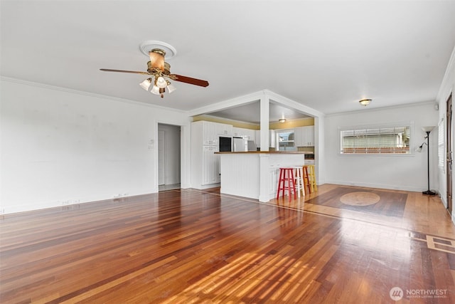 unfurnished living room featuring visible vents, baseboards, ornamental molding, hardwood / wood-style floors, and a ceiling fan