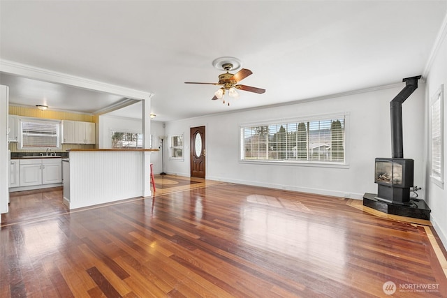 unfurnished living room featuring baseboards, a ceiling fan, wood finished floors, and a wood stove