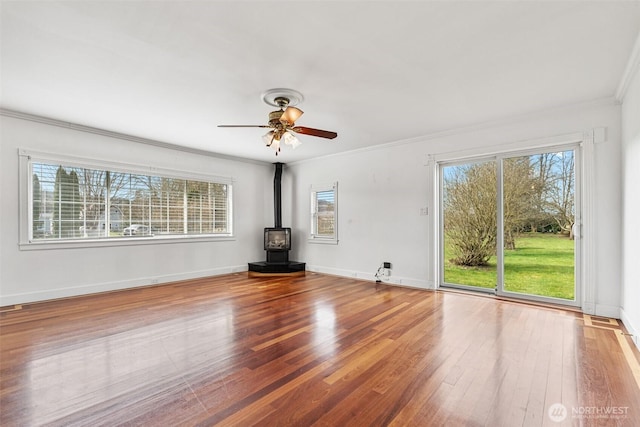 unfurnished room featuring a wealth of natural light, crown molding, a wood stove, and hardwood / wood-style flooring