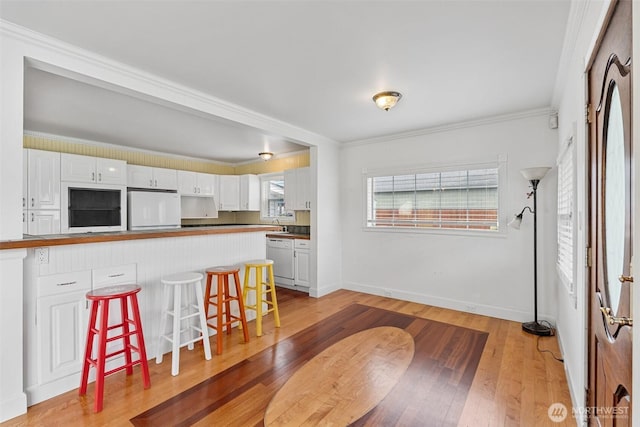 kitchen featuring light wood finished floors, white dishwasher, crown molding, a kitchen bar, and fridge