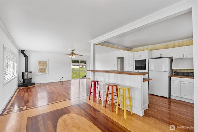 kitchen featuring a breakfast bar, dark countertops, white cabinetry, freestanding refrigerator, and a wood stove