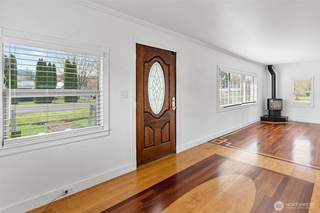 entrance foyer featuring a wood stove, wood finished floors, baseboards, and ornamental molding