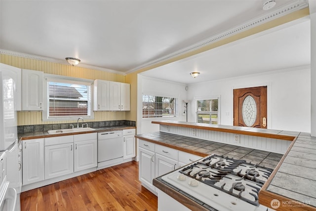 kitchen with white appliances, ornamental molding, a sink, white cabinets, and light wood-type flooring