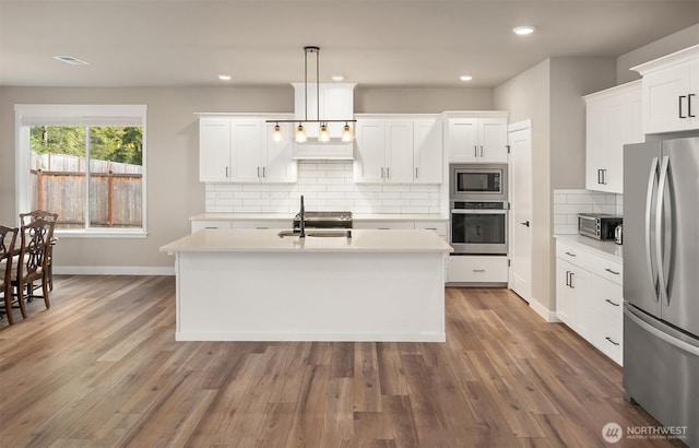 kitchen with a center island with sink, light countertops, appliances with stainless steel finishes, wood finished floors, and a sink