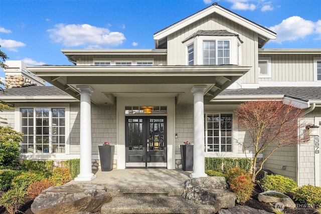 doorway to property featuring french doors, covered porch, and a shingled roof