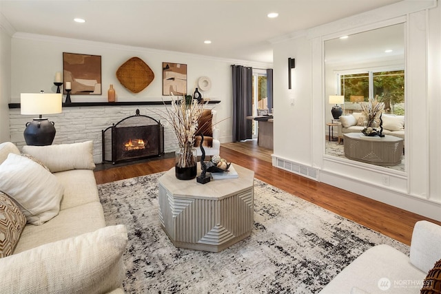 living room featuring visible vents, a stone fireplace, wood finished floors, and crown molding