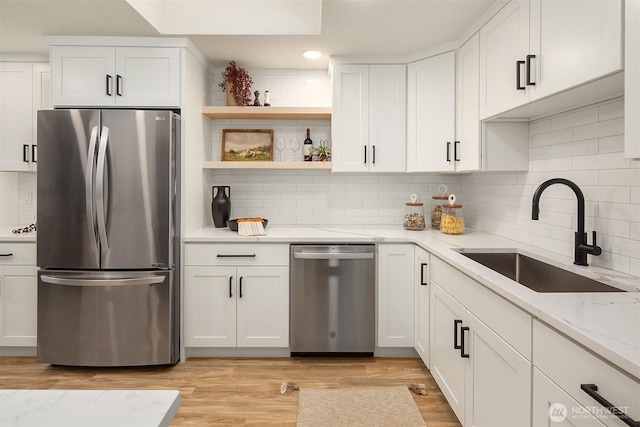 kitchen featuring light wood-style flooring, a sink, light stone counters, appliances with stainless steel finishes, and white cabinets