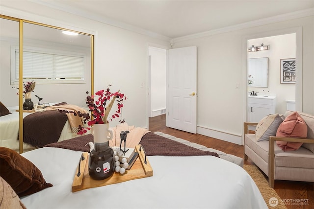 bedroom with ornamental molding, a sink, ensuite bath, wood finished floors, and a closet