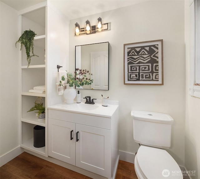 bathroom featuring toilet, vanity, baseboards, and wood finished floors