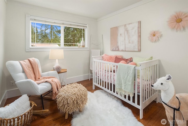 bedroom featuring a crib, baseboards, and wood finished floors