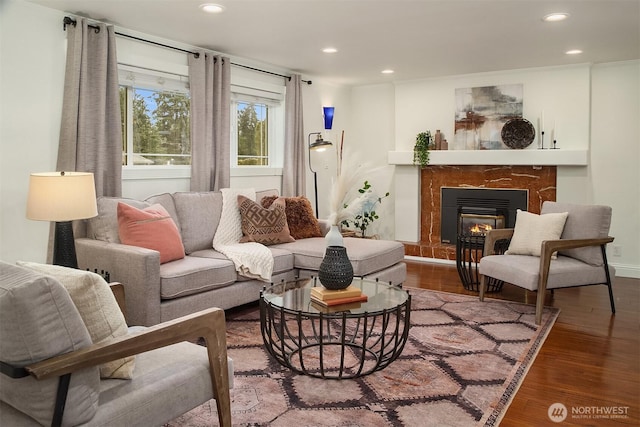 living area with a glass covered fireplace, baseboards, wood finished floors, and recessed lighting