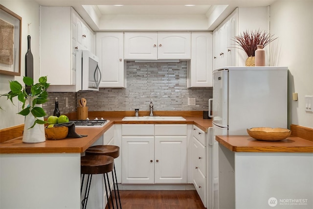 kitchen featuring a sink, stainless steel microwave, backsplash, and white cabinets