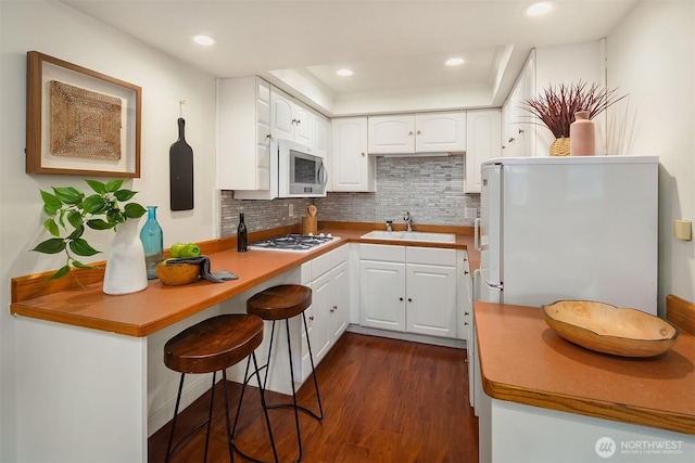 kitchen with white cabinetry, white appliances, dark wood-type flooring, and a sink