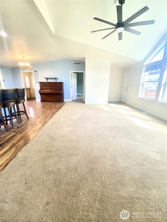 unfurnished living room with visible vents, lofted ceiling, ceiling fan with notable chandelier, carpet floors, and baseboards