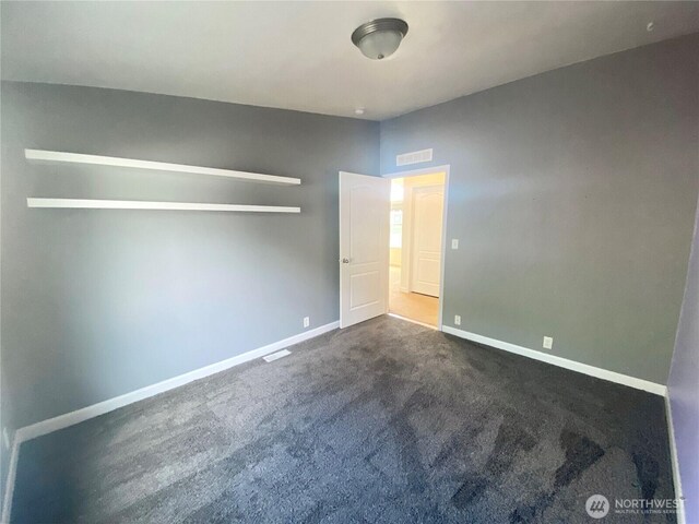 unfurnished bedroom featuring visible vents, dark carpet, and baseboards