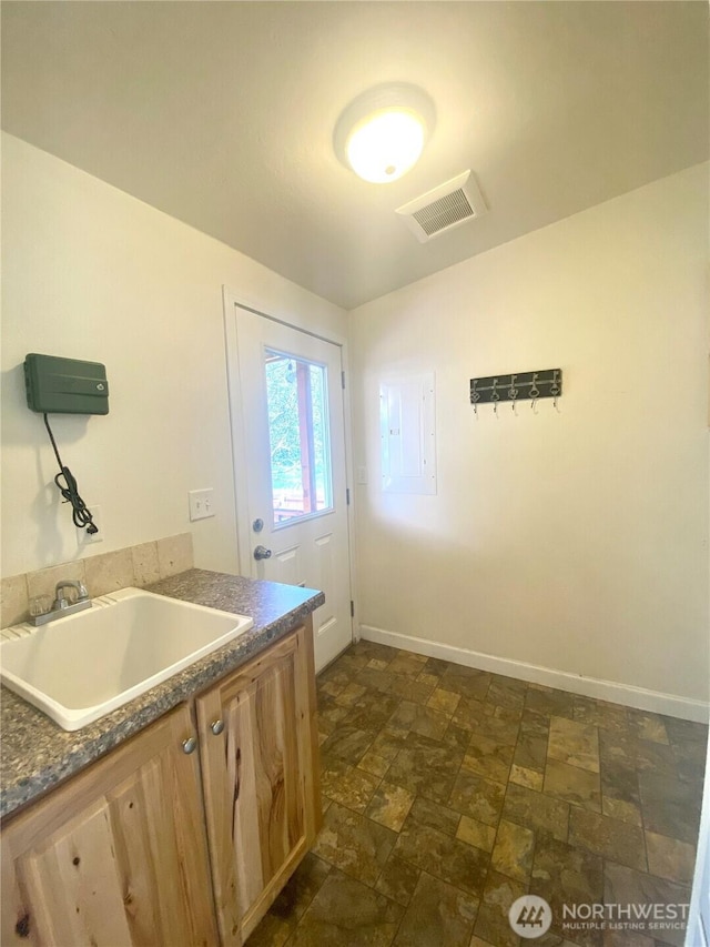 interior space with visible vents, a sink, stone finish flooring, dark countertops, and baseboards