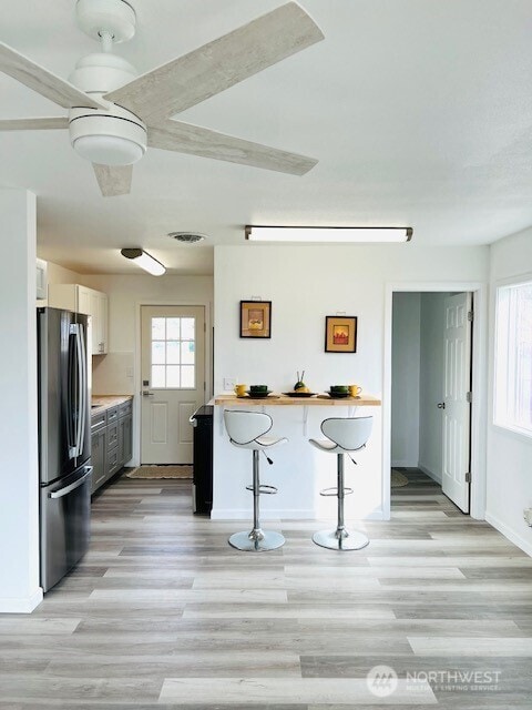 kitchen featuring light wood-style floors, a breakfast bar area, white cabinets, and freestanding refrigerator