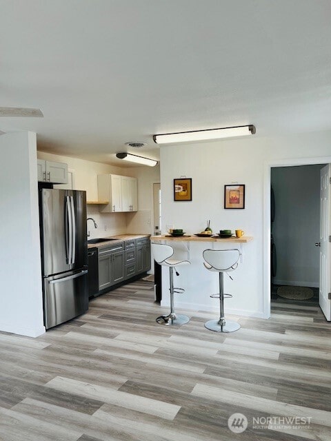 kitchen with a kitchen breakfast bar, light wood-style flooring, freestanding refrigerator, and a sink