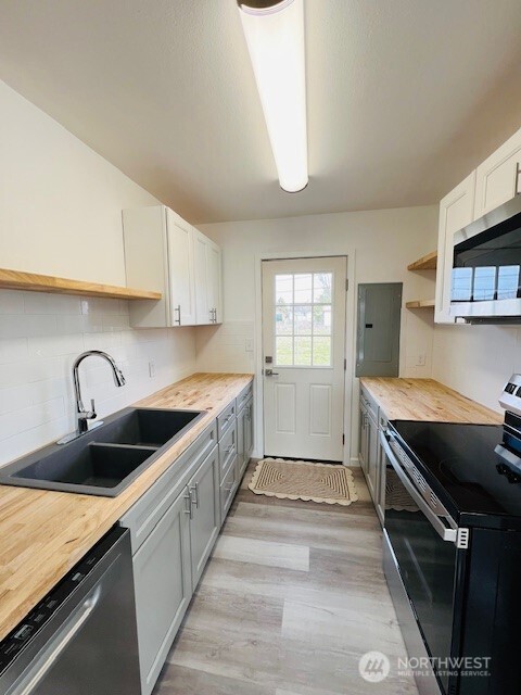 kitchen with backsplash, electric panel, light wood-style flooring, stainless steel appliances, and a sink