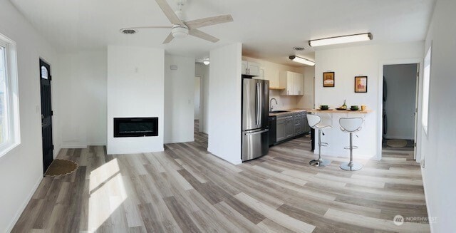 kitchen with light countertops, light wood-style flooring, freestanding refrigerator, a glass covered fireplace, and a sink