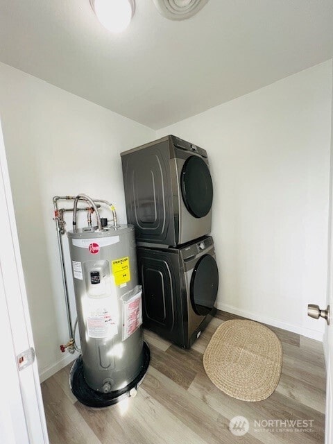 laundry area featuring laundry area, wood finished floors, water heater, and stacked washing maching and dryer