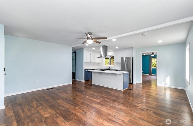 kitchen featuring a kitchen island, a breakfast bar, freestanding refrigerator, light countertops, and island range hood