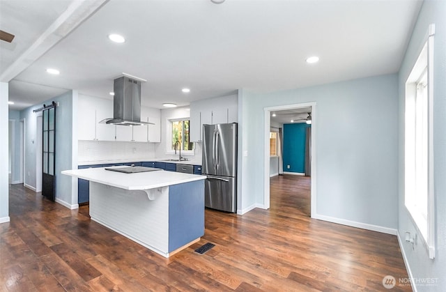 kitchen with freestanding refrigerator, a sink, light countertops, a barn door, and island range hood