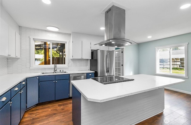 kitchen with light countertops, appliances with stainless steel finishes, island range hood, blue cabinets, and a sink