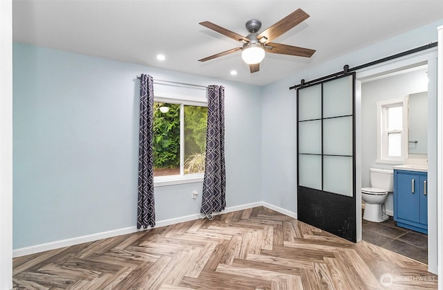 unfurnished bedroom featuring a barn door, recessed lighting, baseboards, and connected bathroom