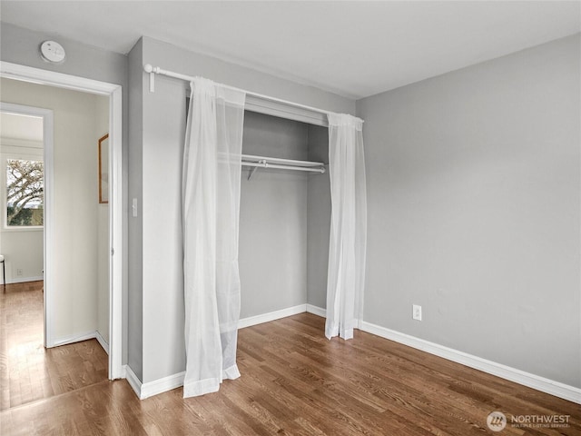 unfurnished bedroom with a closet, baseboards, and wood finished floors