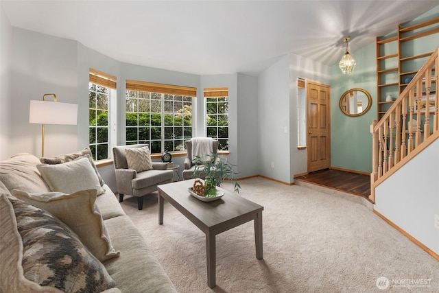 carpeted living area featuring stairs, an inviting chandelier, and baseboards