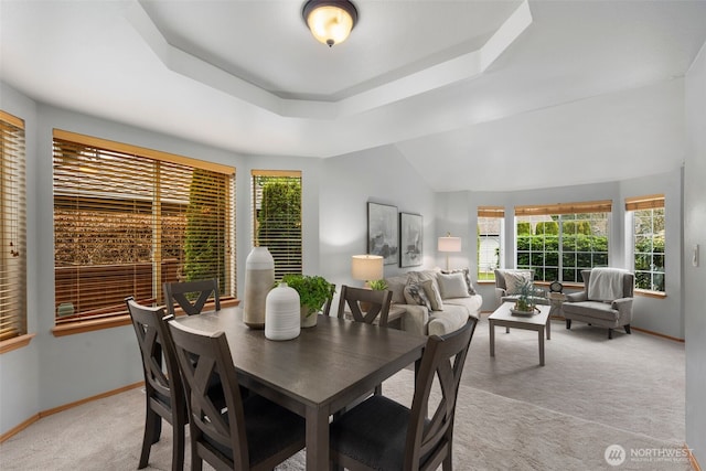 dining area with a tray ceiling, light colored carpet, and baseboards