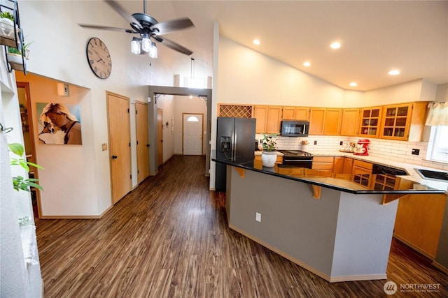 kitchen featuring black appliances, a breakfast bar area, glass insert cabinets, and dark wood-type flooring