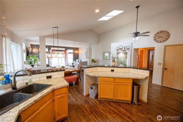 kitchen with dark wood finished floors, open floor plan, lofted ceiling with skylight, pendant lighting, and a sink