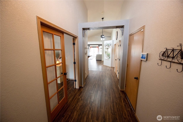 hallway with french doors, dark wood-type flooring, a textured wall, and vaulted ceiling