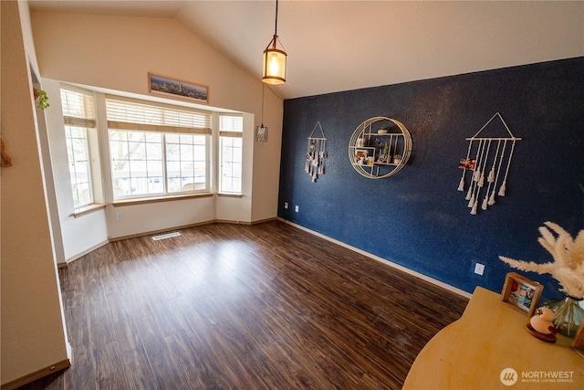 interior space with visible vents, lofted ceiling, wood finished floors, baseboards, and an accent wall