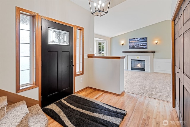 entrance foyer featuring lofted ceiling, a notable chandelier, a fireplace with flush hearth, and light wood-style floors