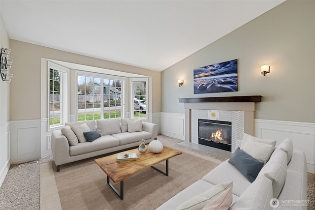 living area featuring visible vents, wainscoting, a fireplace, and vaulted ceiling